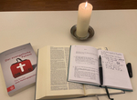 Buch "Der evangelische Patient" neben offener Bibel und Losung , Notizbuch, Stift und brennender Kerze